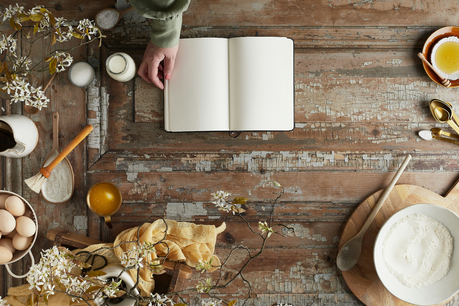 an blank notebook site on a wooden table and someone prepares to write a recipe